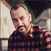 Paul wearing a red and black check shirt, smiling at the camera